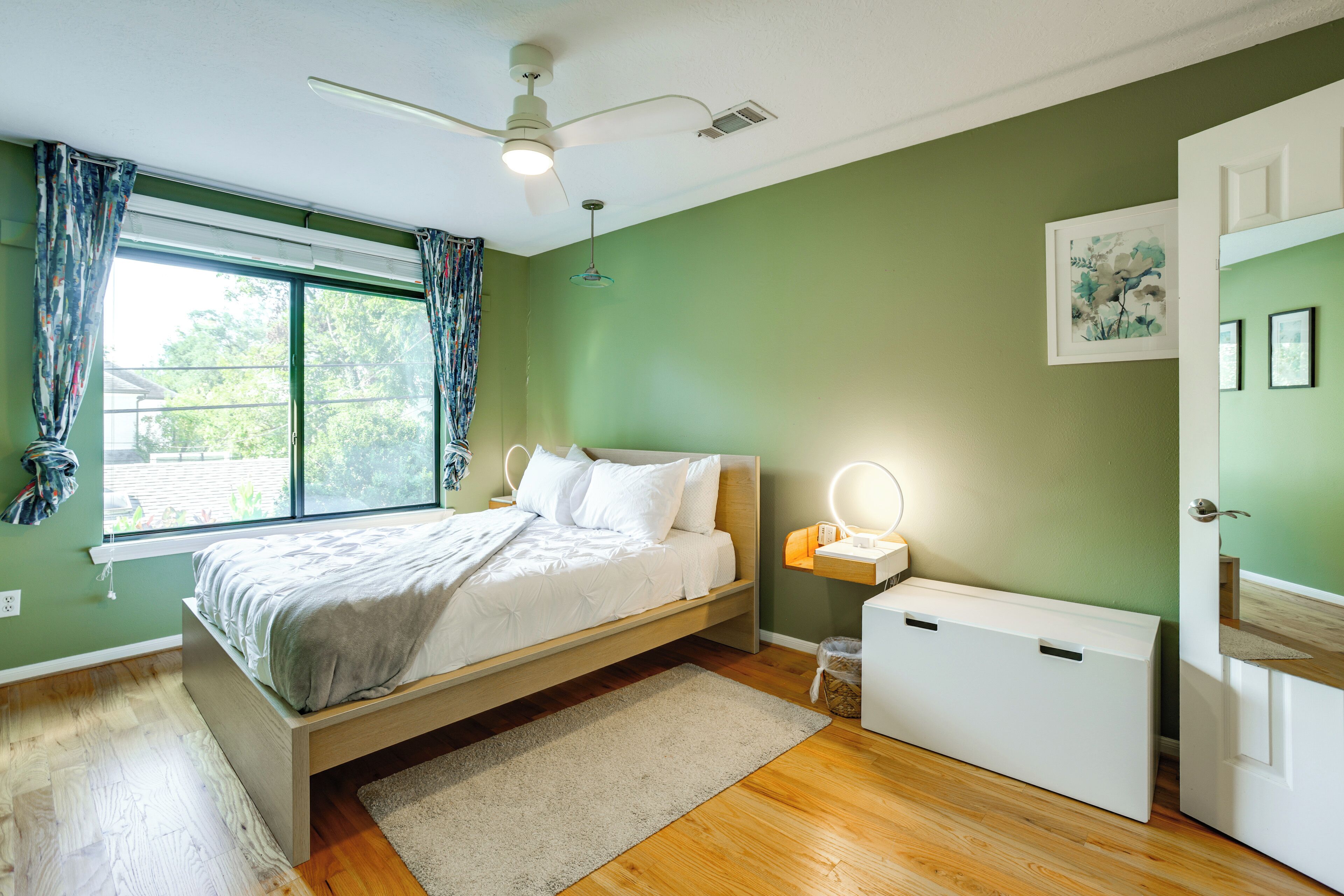 Une chambre à coucher avec un lit, une table de chevet avec une lampe, un radiateur et une fenêtre avec des rideaux.