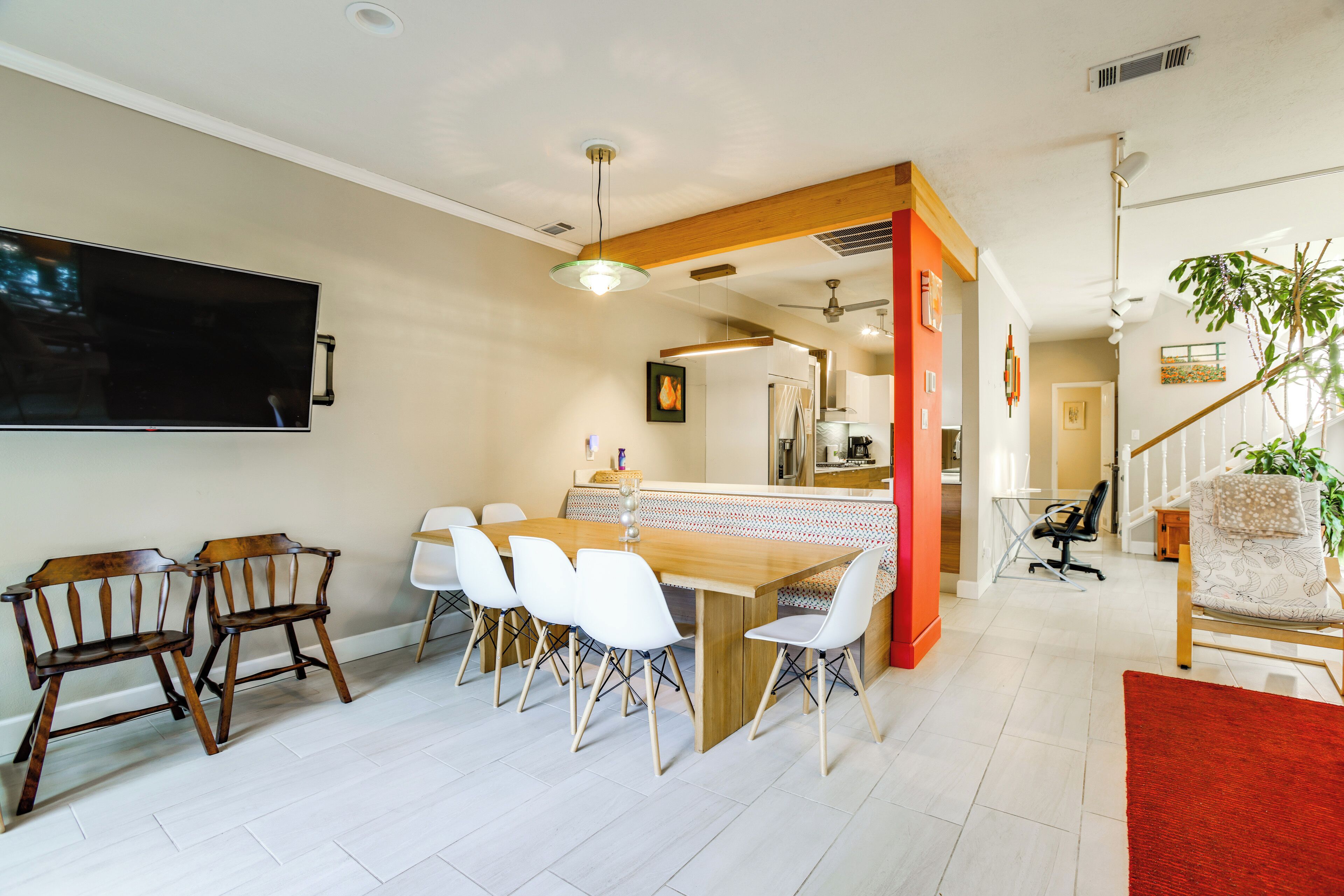 Een eetgedeelte met een houten tafel en stoelen, een aan de muur bevestigde televisie, en een trap naar een hoger niveau.