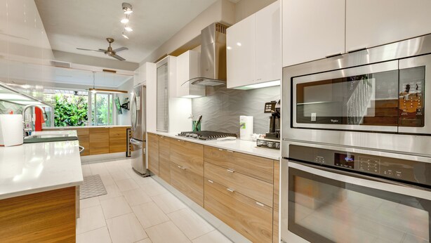A modern kitchen with stainless steel appliances, wooden cabinets, and a large window overlooking greenery.