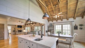 A spacious kitchen with a large island, wooden ceiling beams, pendant lighting, and a stone fireplace. - Deck + Fire Pits: Lake Toxaway Getaway! (Lake Toxaway)