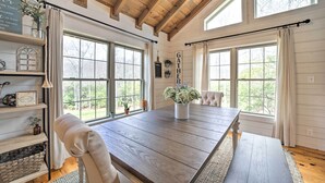 A dining room with a wooden table, chairs, and a bench. There are windows with curtains, a shelf with decorative items, and a sign that says "GATHER". - Deck + Fire Pits: Lake Toxaway Getaway! (Lake Toxaway)