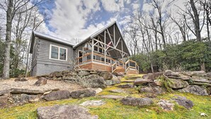A cabin with a stone foundation, wooden deck, and a large window. - Deck + Fire Pits: Lake Toxaway Getaway! (Lake Toxaway)