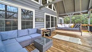 A covered porch with a blue sofa, wicker ottoman, and a bench. - Deck + Fire Pits: Lake Toxaway Getaway! (Lake Toxaway)