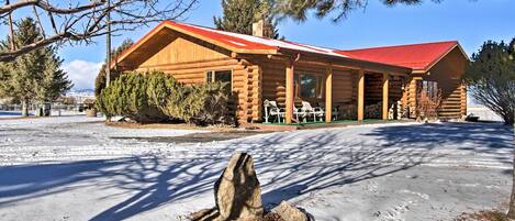 A log cabin with a red roof, a covered porch, and a snow-covered ground.