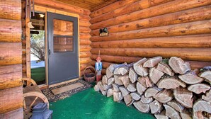 A log cabin interior with a door, a stack of firewood, and a wooden wheel. - Secluded Dillon Home w/ Private Hot Tub + Deck! (Dillon)