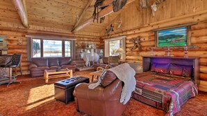 A log cabin interior with a large bed, leather sofa, and a fireplace. - Secluded Dillon Home w/ Private Hot Tub + Deck! (Dillon)