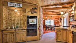 A log cabin kitchen with a stone wall, wooden cabinets, a stove, and a dining area with a table and chairs. - Secluded Dillon Home w/ Private Hot Tub + Deck! (Dillon)