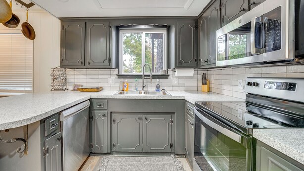 A modern kitchen with grey cabinets, a stainless steel sink, and a built-in oven. - Beaver Lake Home ~ 8 Mi to Downtown Rogers! (Rogers)