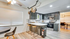 A modern kitchen with a central island, bar stools, a ceiling fan, and a trash can. - Beaver Lake Home ~ 8 Mi to Downtown Rogers! (Rogers)