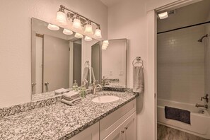 A bathroom with a granite countertop, a sink, a mirror with lights, a towel rack, and a shower area.