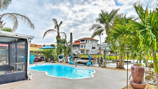 A swimming pool with a curved edge, surrounded by palm trees and a covered patio area with outdoor furniture. - Pet-friendly Hudson Home: Boat Slip, Private Pool (Hudson)