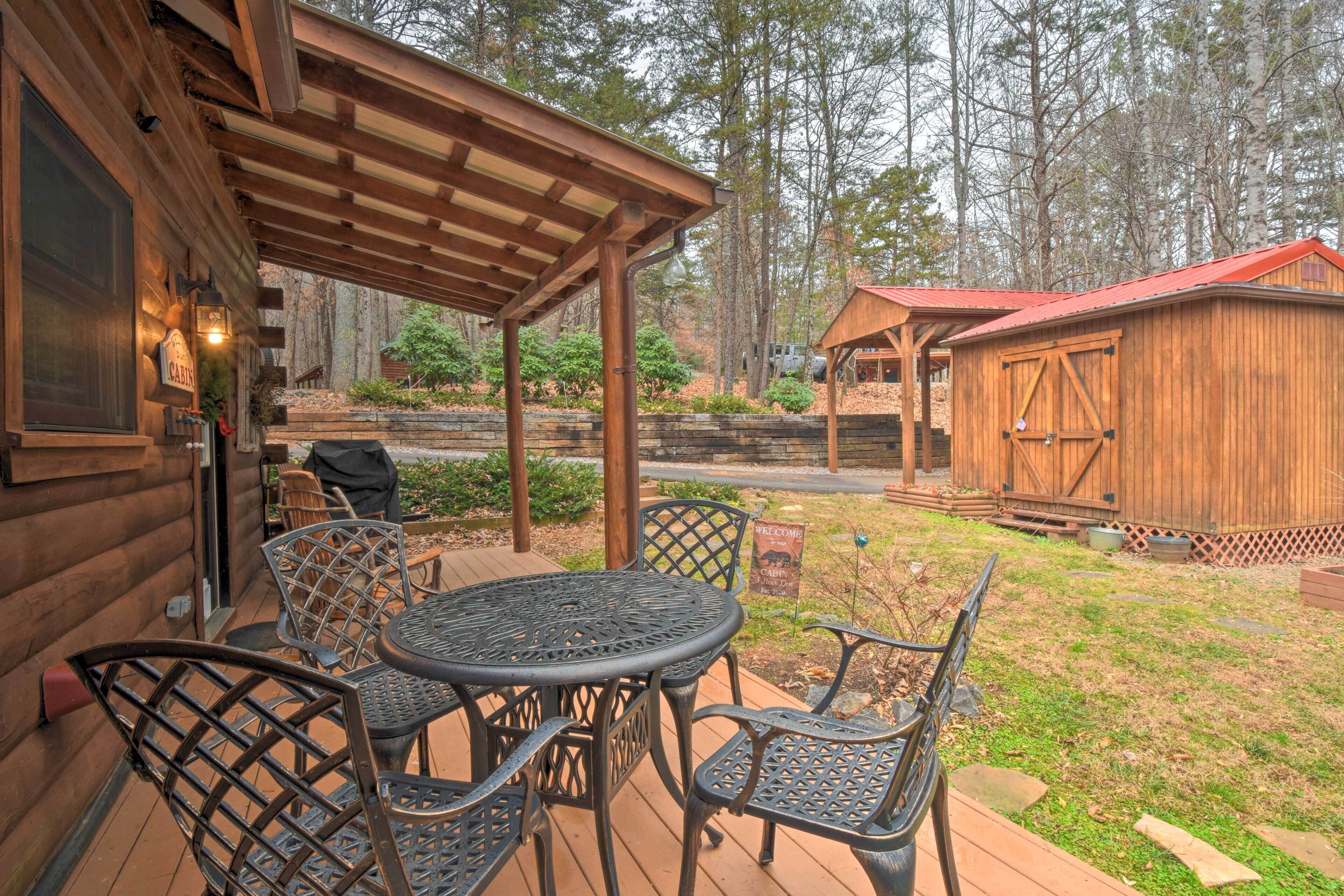A wooden cabin with a patio area featuring a round table and chairs, a covered seating area, and a small shed.
