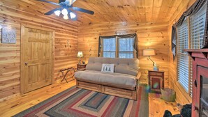 A cozy log cabin room with a wooden ceiling, a ceiling fan, a sofa, a window with curtains, and a small table with a lamp. - Rural Murphy Cabin - Yard, Hot Tub & Fire Pit (Murphy)