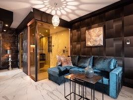 A modern living room with a blue velvet sofa, a marble floor, and a geometric wall art piece.