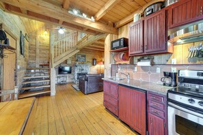 A wooden cabin interior with a kitchen, dining area, and a stone fireplace. - Private Hot Tub: 'blue Sky Cabin' in Sequim (Sequim)