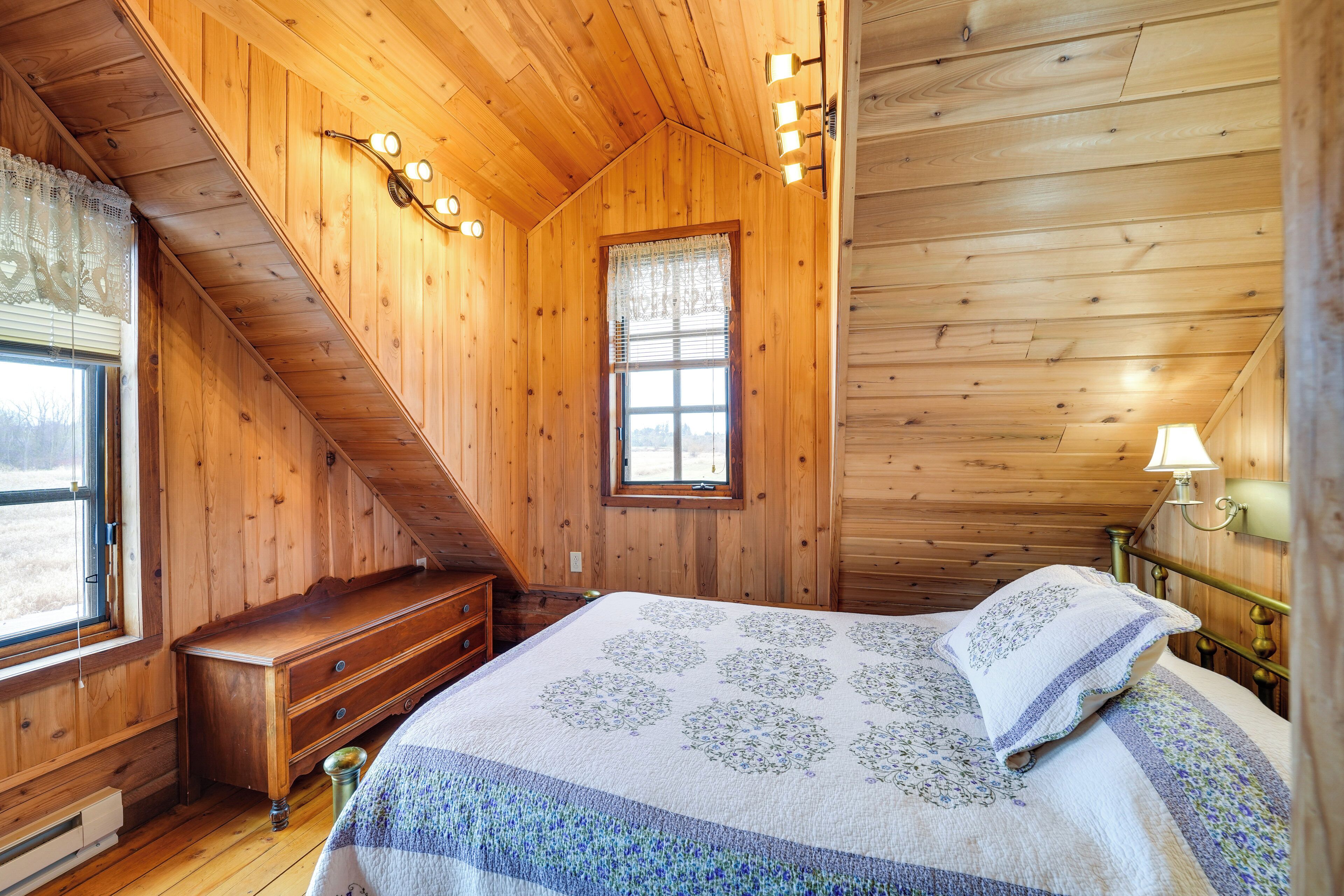 A wooden cabin bedroom with a bed, a dresser, and a window with a curtain.