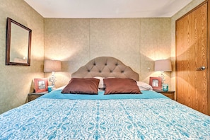 A bedroom with a tufted headboard, a patterned bedspread, two bedside tables with lamps, and a wooden wardrobe.