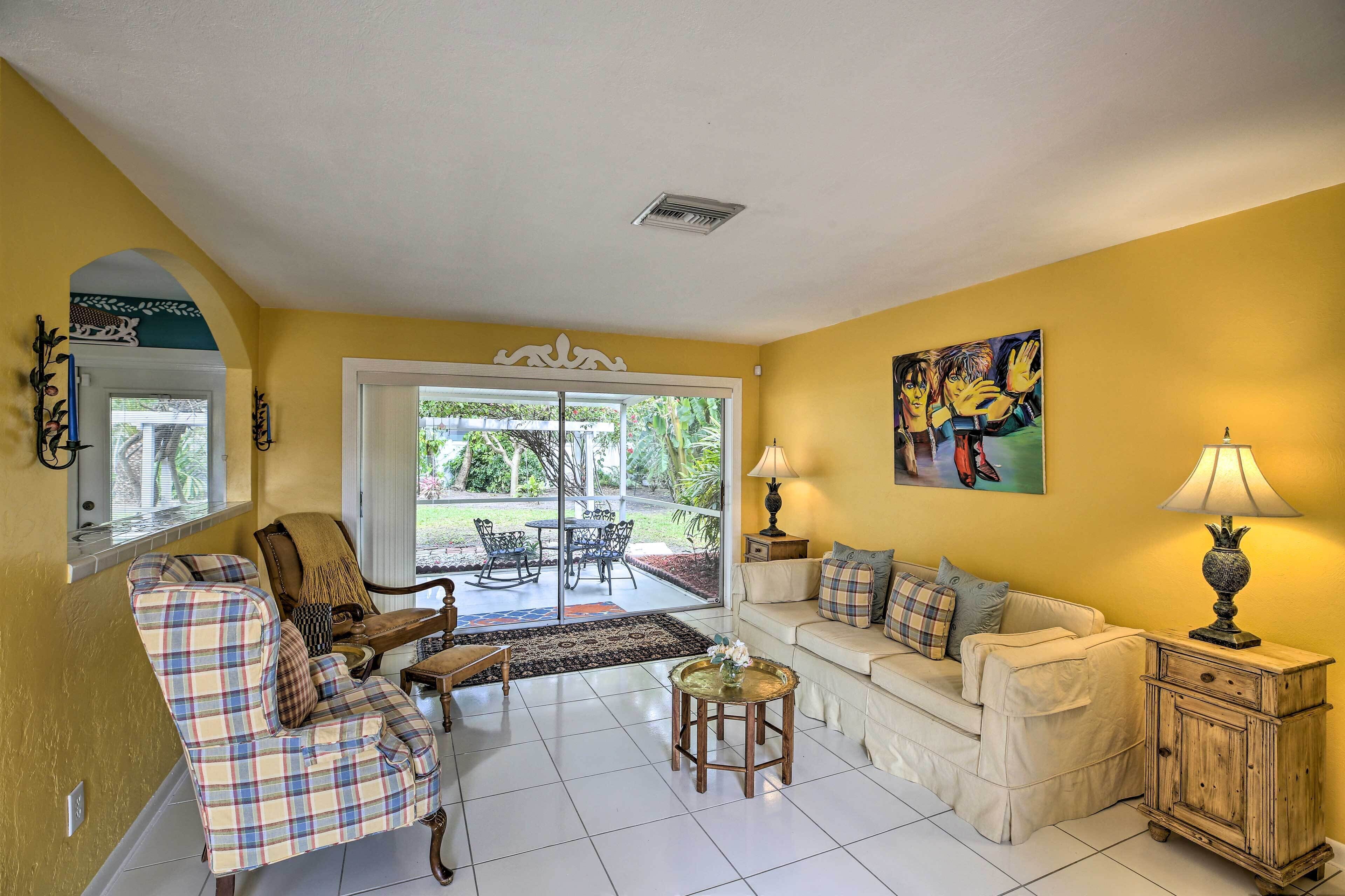 A living room with a sofa, armchair, and coffee table, a dining area with chairs and a table, and a painting on the wall.