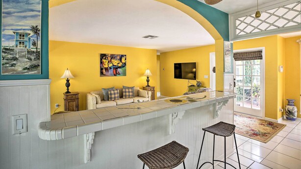 A kitchen with a curved island, yellow walls, and a large window. - Cape Coral Home w/ Yard < 1 Mi to Dtwn! (Cape Coral)