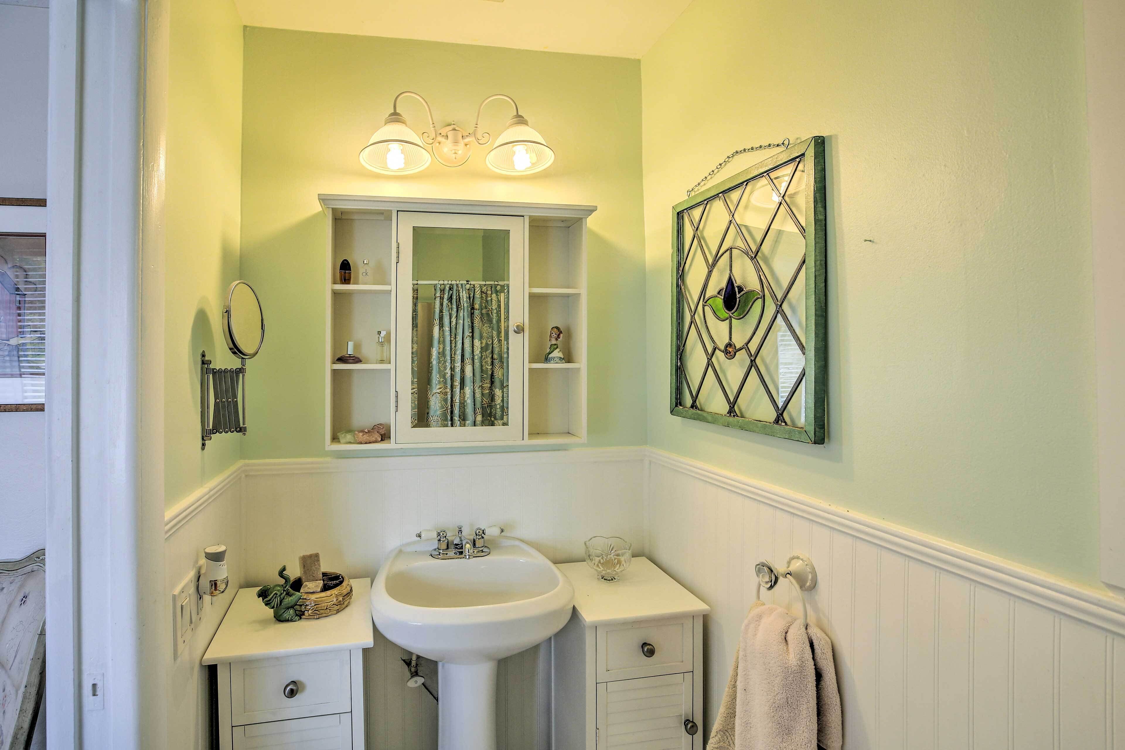 Une salle de bain avec un lavabo blanc, un meuble-lavabo et un placard, un miroir et une fenêtre décorative en vitrail.