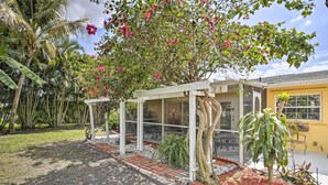 A covered outdoor seating area with a white pergola, surrounded by tropical plants and a yellow building in the background. - Cape Coral Home w/ Yard < 1 Mi to Dtwn! (Cape Coral)