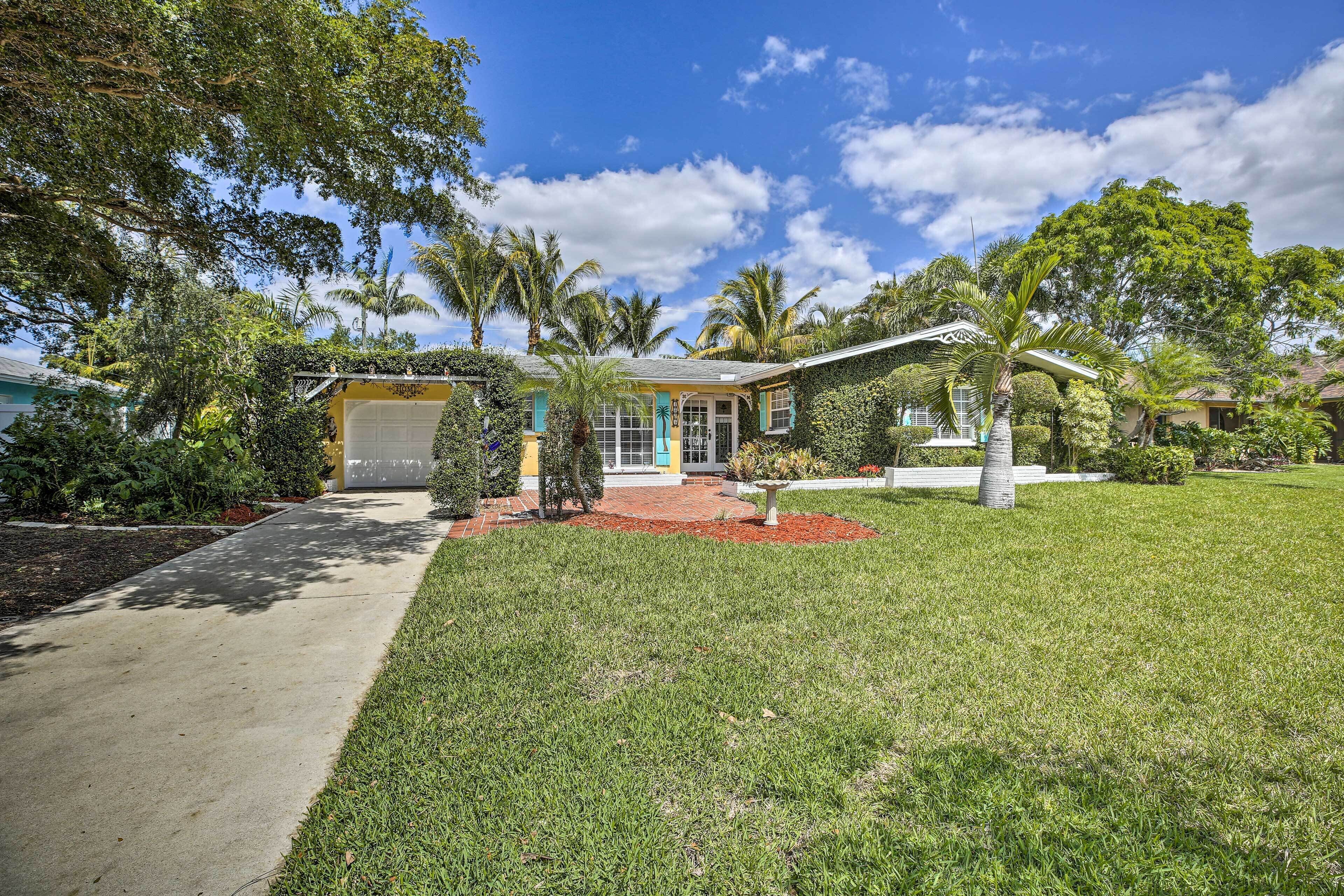 A residential house with a well-maintained lawn, palm trees, and a clear blue sky.