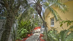 A narrow pathway flanked by lush greenery and a yellow building. - Cape Coral Home w/ Yard < 1 Mi to Dtwn! (Cape Coral)