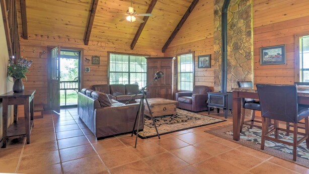 A spacious living room with a wooden ceiling, a fireplace, and a stone accent wall. - On Farm: Rustic Carmine Log Cabin w/ Porch! (Carmine)