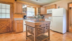 A kitchen with wooden cabinets, a central island with drawers, a refrigerator, and a window with blinds. - On Farm: Rustic Carmine Log Cabin w/ Porch! (Carmine)