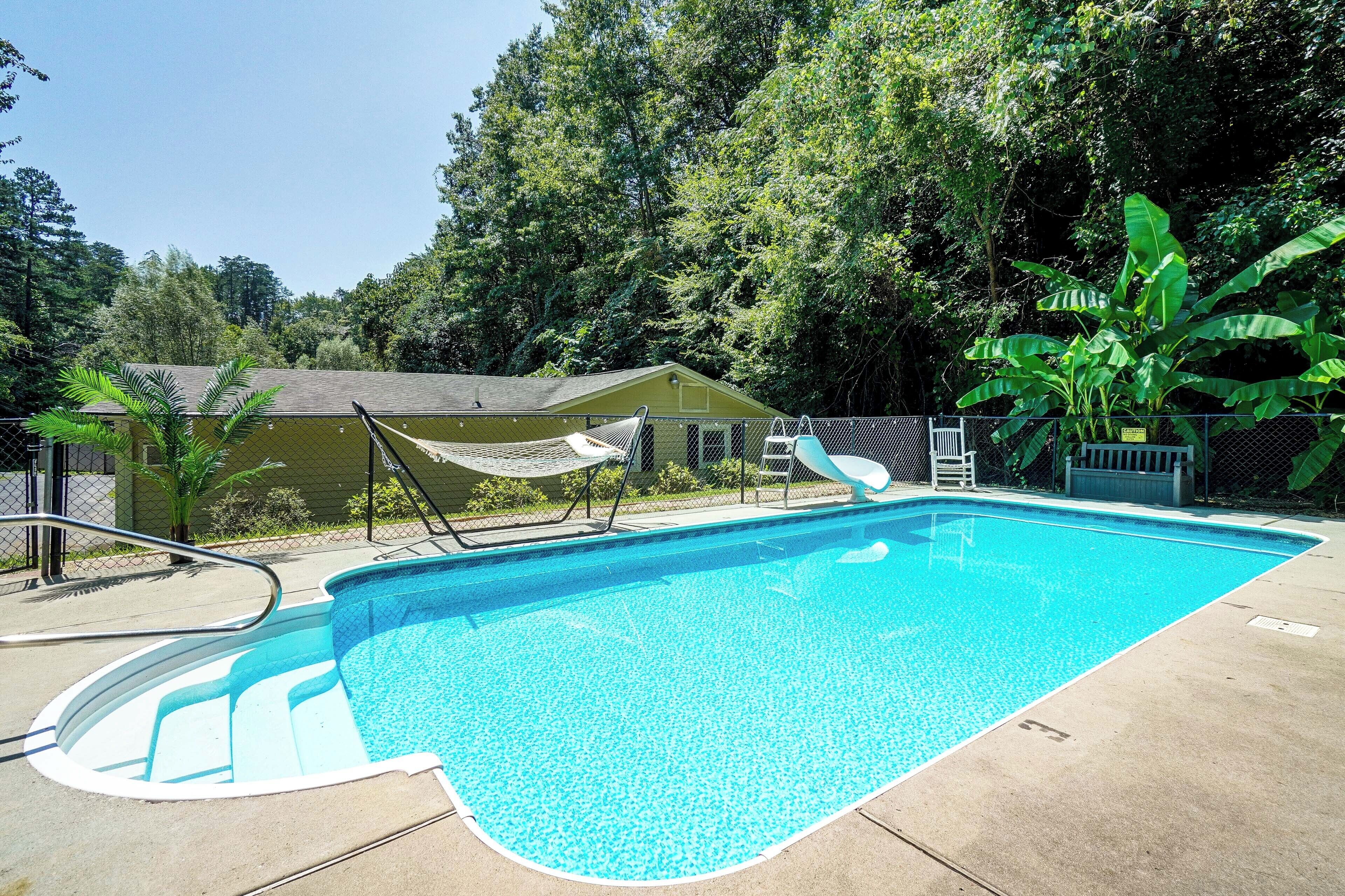 A swimming pool with a diving board and a hammock.