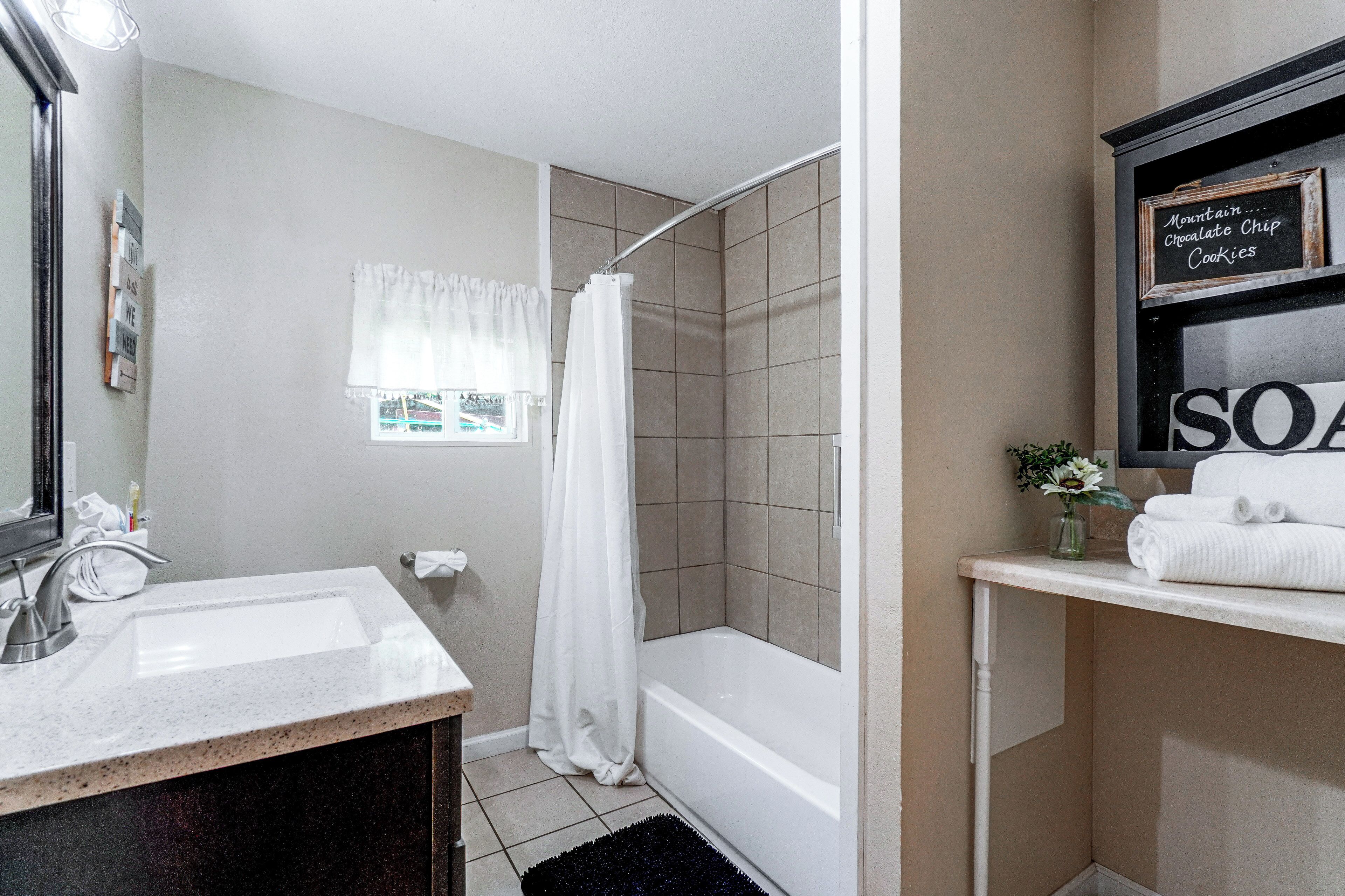 A bathroom with a sink, mirror, shower, and a shelf with towels and a sign.