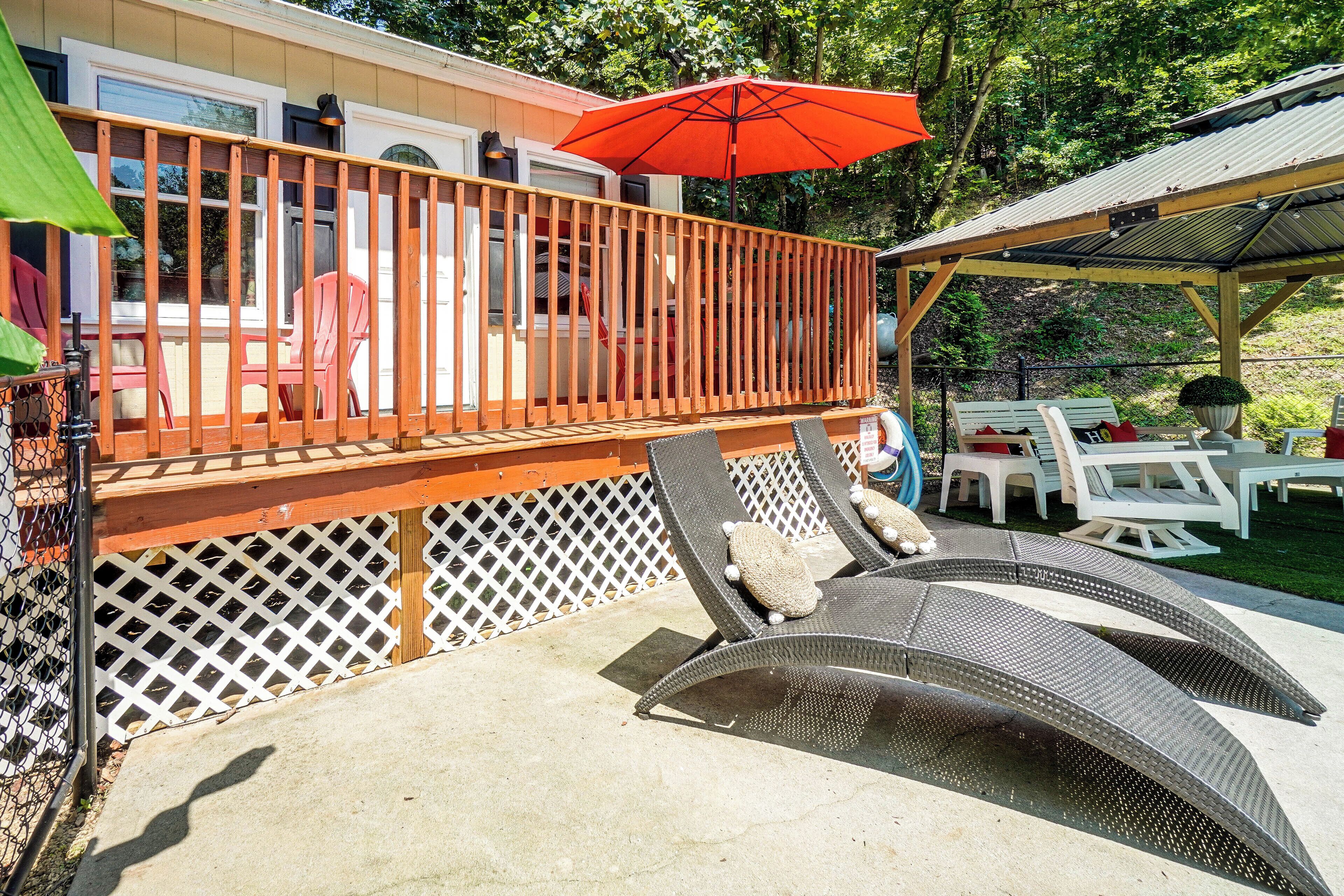 A covered outdoor deck with a wooden railing, lounge chairs, and a red umbrella.