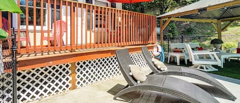 Une terrasse extérieure couverte, dotée d’une rambarde en bois, de chaises longues et d’un parasol rouge.