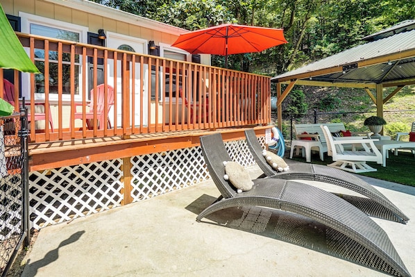 A covered outdoor deck with a wooden railing, lounge chairs, and a red umbrella.