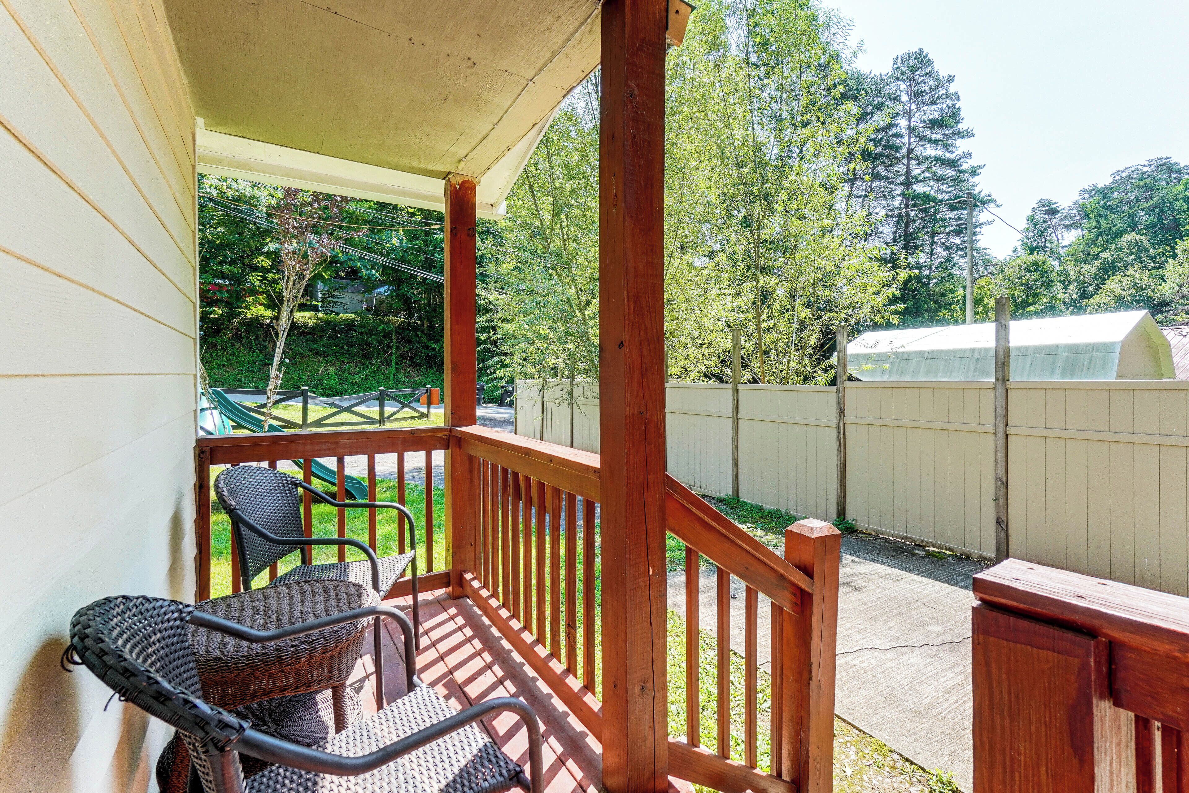 A covered outdoor area with a wooden deck, two wicker chairs, and a table.