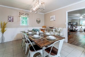 Un comedor con una mesa de madera dispuesta para cuatro, sillas blancas y una lámpara colgante.