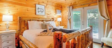 A wooden cabin bedroom with a bed, nightstands, a ceiling fan, and a window with curtains.