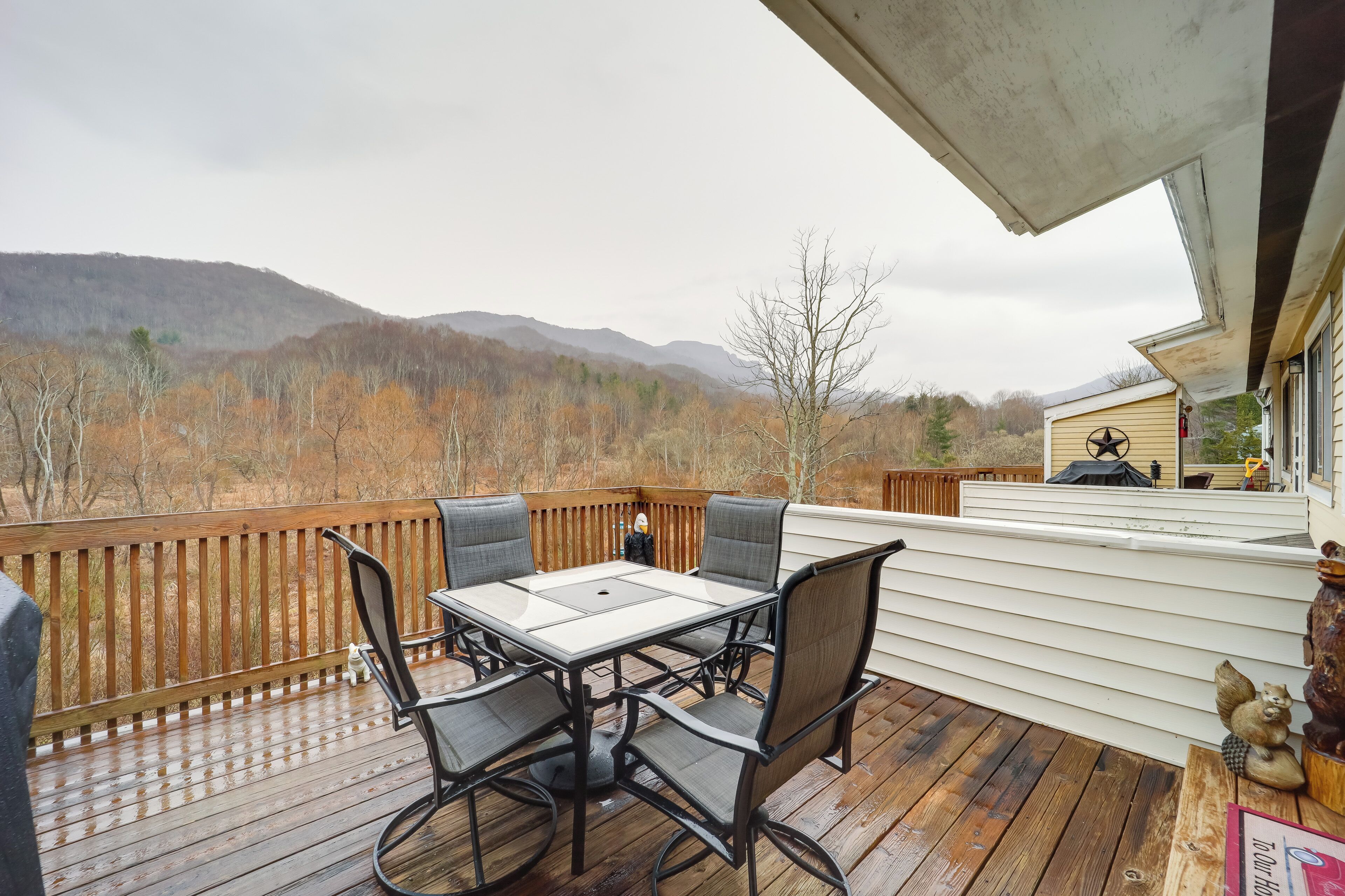 A wooden deck with a table and chairs, overlooking a mountainous landscape.