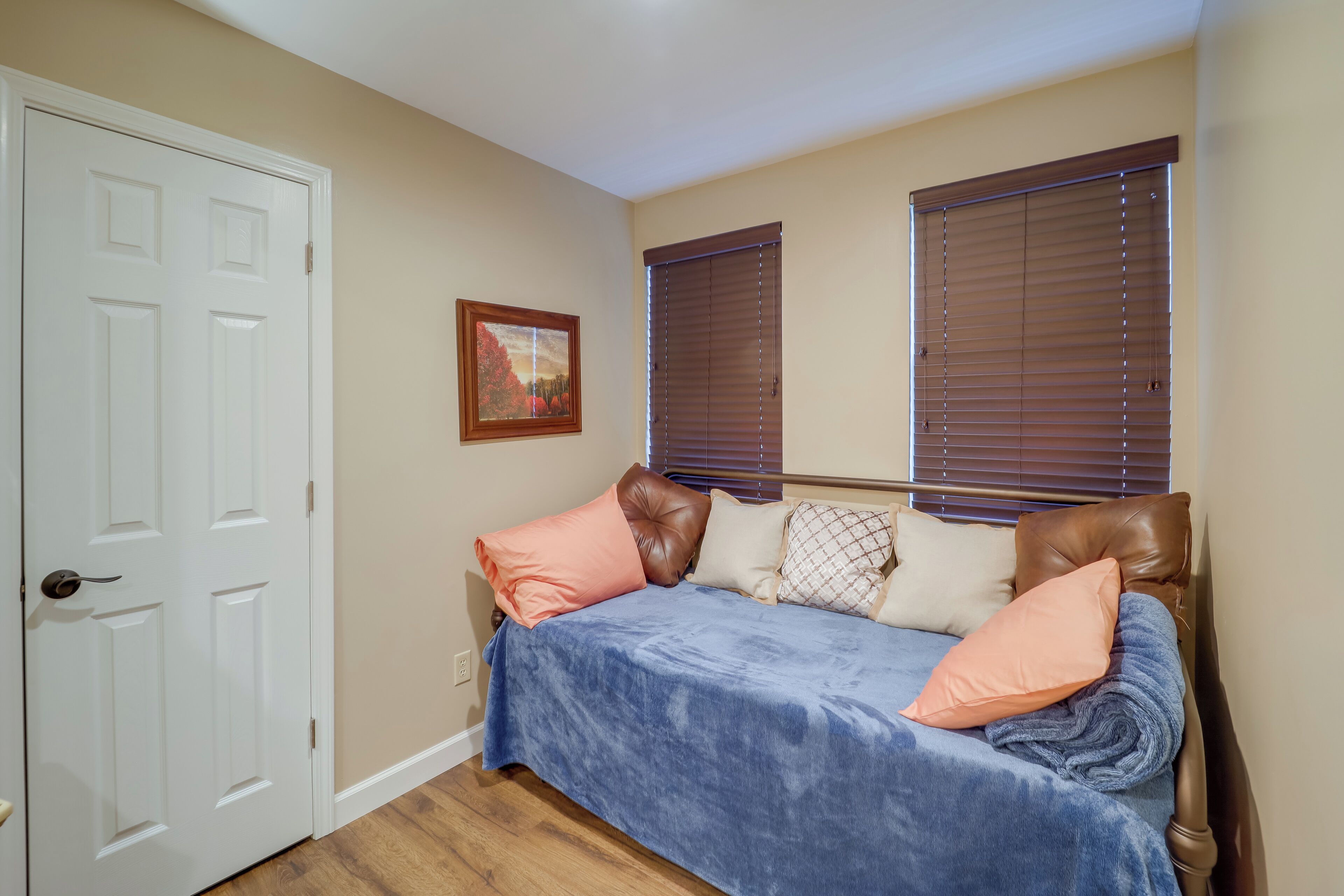 A bedroom with a bed, a door, and two windows with blinds.