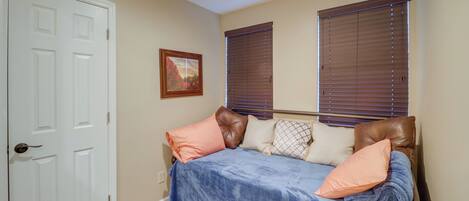 A bedroom with a bed, a door, and two windows with blinds.