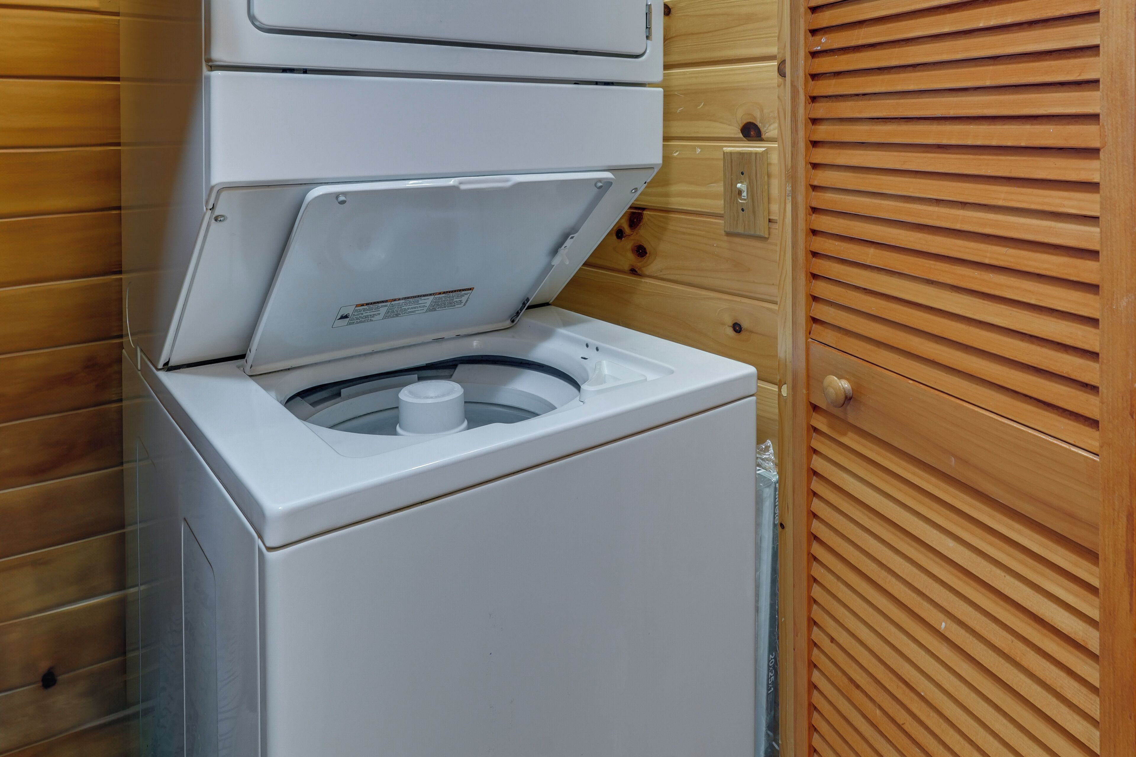 Una lavadora compacta y blanca en una habitación tipo cabaña, con puerta y paneles de madera.