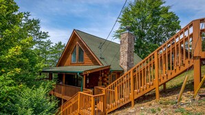 A log cabin with a stone chimney, wooden deck, and a staircase. - The Dreamer's Nest Sevierville Cabin w/ Hot Tub! (Sevierville)