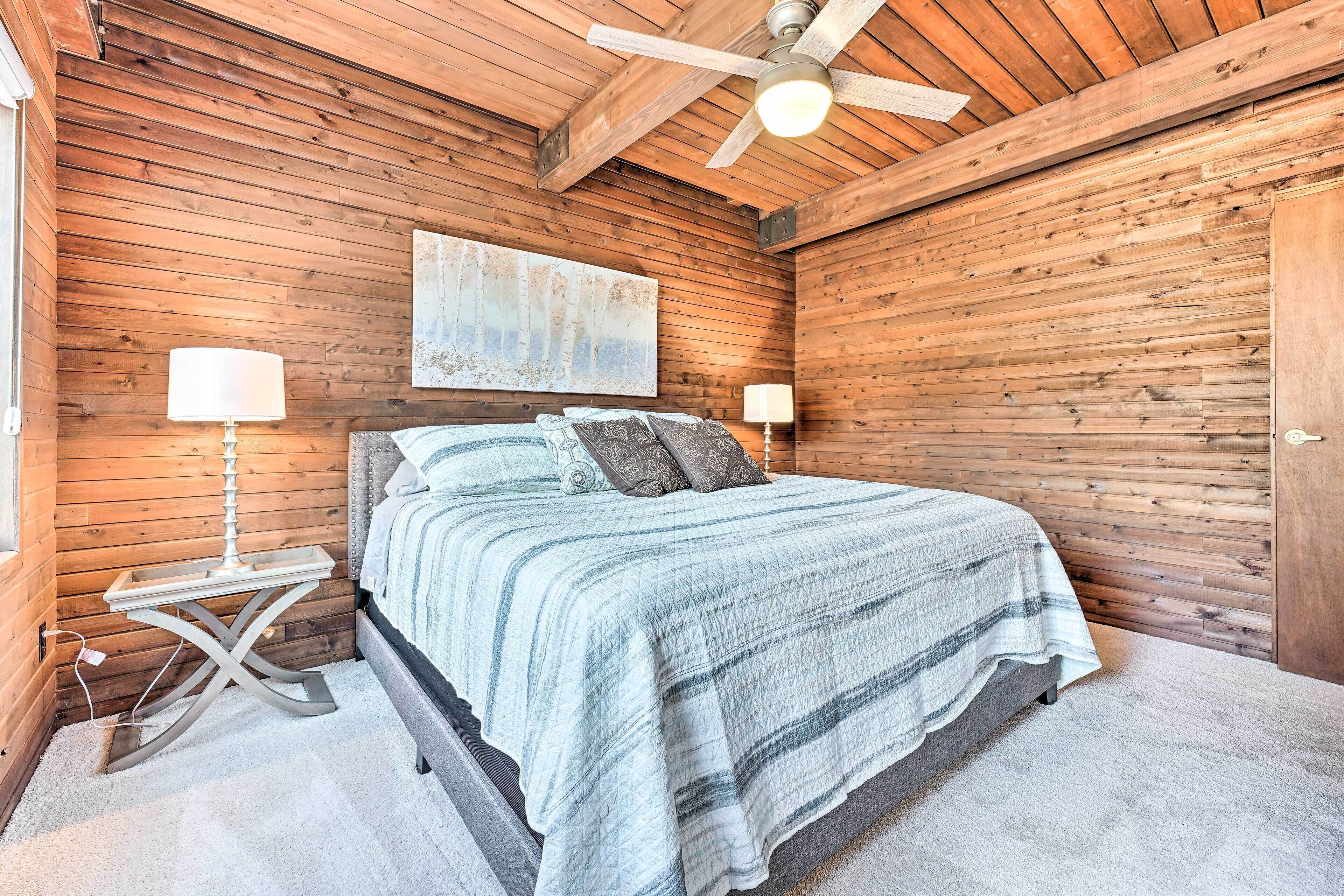 Une chambre à coucher avec un lit, deux lampes de chevet, un ventilateur de plafond et un mur en bois.