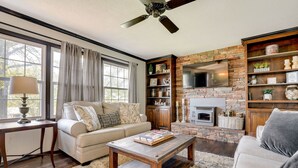 A living room with a fireplace, a sofa, a coffee table, and a TV. - Charming Shell Knob Home: 16 Mi to Dogwood Canyon! (Shell Knob)