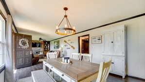 A dining area with a wooden table, white chairs, a chandelier, and a white cabinet. - Charming Shell Knob Home: 16 Mi to Dogwood Canyon! (Shell Knob)