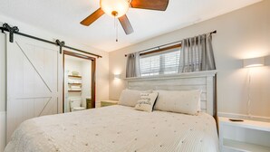 A bedroom with a bed, a ceiling fan, a window with curtains, a nightstand, and a bedside table. - Charming Shell Knob Home: 16 Mi to Dogwood Canyon! (Shell Knob)