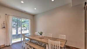 Un coin repas avec une table en bois et des chaises blanches, un banc et une plante en pot.