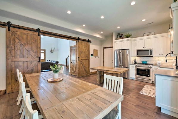 A spacious kitchen with wooden flooring, white cabinets, a large wooden dining table, and modern appliances.