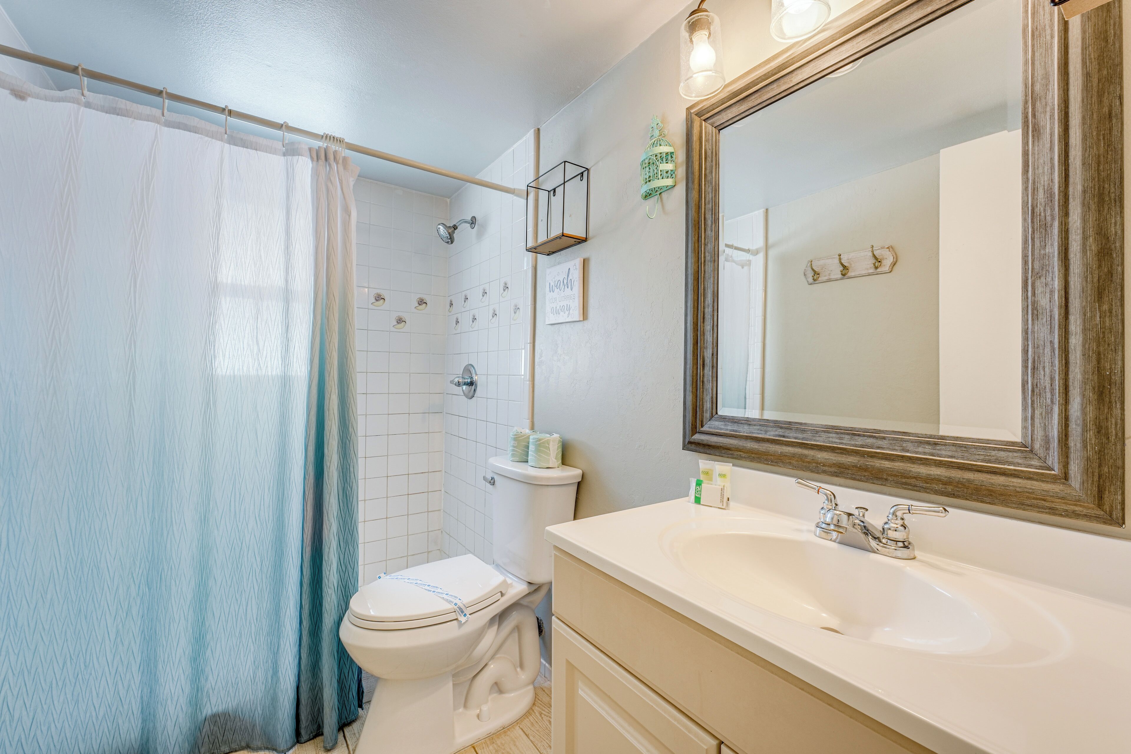 Une salle de bain équipée d’un rideau de douche, de toilettes, d’un lavabo et d’un miroir.