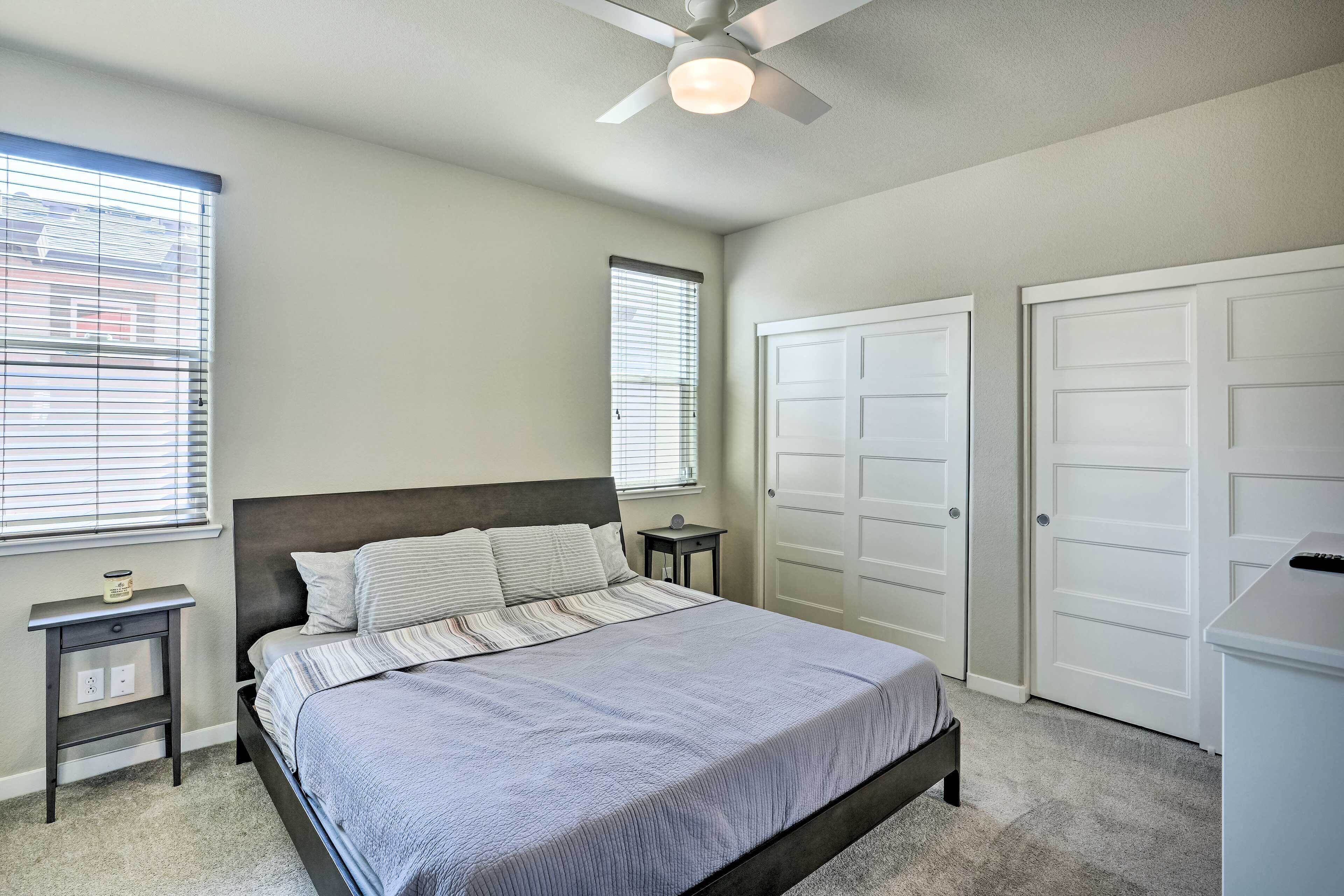 Une chambre à coucher comprenant un lit, deux tables de chevet, un ventilateur de plafond et deux portes.